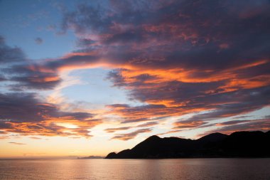 Gün batımında gökyüzü ve bulutların arasında güneş olan sakin bir deniz. Meditasyon okyanusu ve gökyüzü arka planı. Huzurlu deniz manzarası 