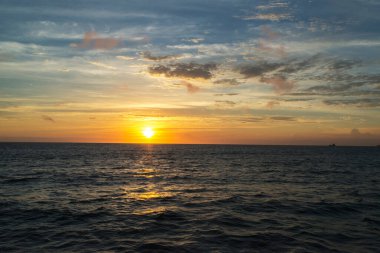 Deniz üzerinde güzel bir gün batımı, bulutlu bir gökyüzü