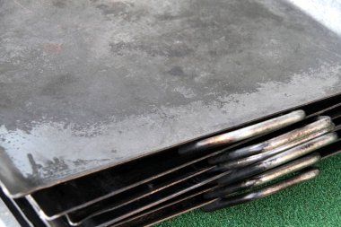 Yığılmış metal pişirme tepsileri yeşil yüzeyde duruyor.