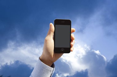 Mavi gökyüzü arka planında boş ekranlı akıllı telefonu tutan kişinin kırpılmış görüntüsü