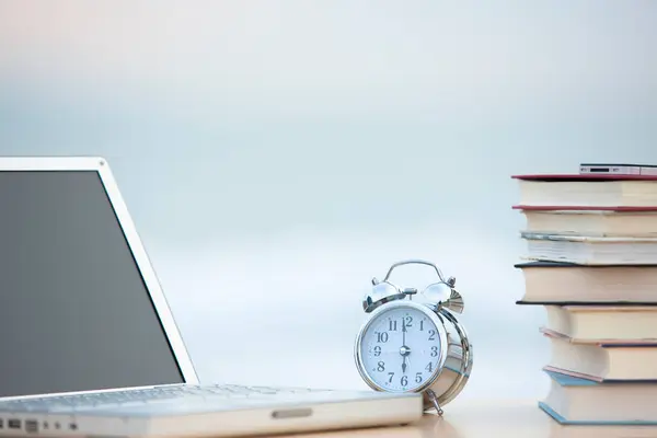close up laptop, stack of books and clock on sea shore
