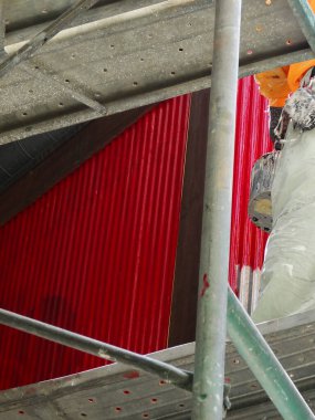 Açık havada sprey ekipman kullanarak parlak kırmızı kıvrımlı metal duvar boyuyor.