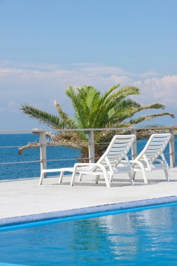 Güneş yatakları ve mavi deniz manzaralı boş yüzme havuzu alanı 