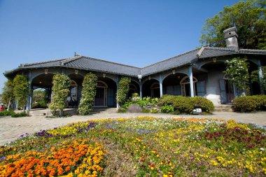 Mavi gökyüzünün altında renkli çiçeklerle çevrili tarihi bir ev.