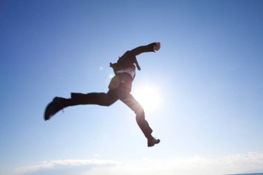 Mavi gökyüzü arka planında siyah takım elbiseli Japon adam dışarı atlıyor. 