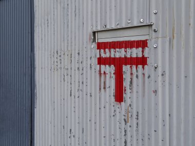 Yıpranmış metal duvara kırmızı grafiti sembolü çizilmiş.