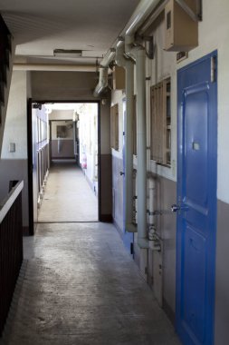 Mavi kapıları ve boruları olan dar apartman koridoru.