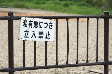 Paslı metal çitler kumlu bölgeyi Japon uyarı levhasıyla kapatıyor.