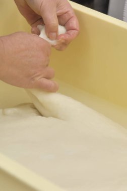 Sarı kabın içinde yumuşak hamuru geren eller