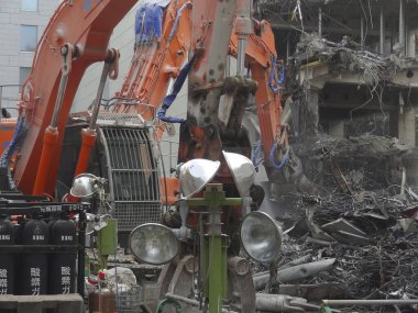 Turuncu kazıcılar etrafa saçılmış enkazlarla hasarlı binayı yıkıyor.