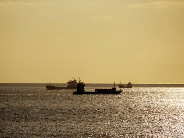 Kargo gemileri sakin altın okyanus sularında yüzüyor.