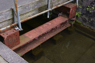 Paslı metal kiriş sığ suyu dışarıda beton duvarın yanında geçiyor.