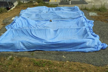 Açık alandaki inşaat malzemelerini kapsayan büyük mavi brandalar.