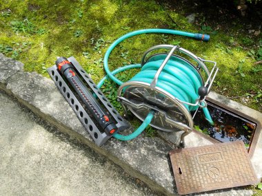 Yeşil bahçe hortumu, beton yürüyüş yolunun yanında güzelce sarılmış.