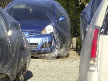 Açık havada park halindeki araçların arasında plastikle kaplı mavi bir araba.