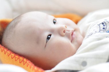 Yatağa uzanmış Asyalı bebek portresi.