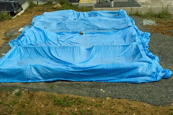 Açık alandaki inşaat malzemelerini kapsayan büyük mavi brandalar.