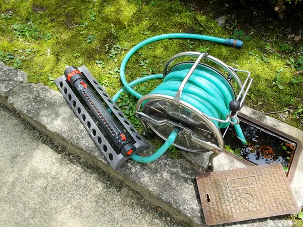 Yeşil bahçe hortumu, beton yürüyüş yolunun yanında güzelce sarılmış.