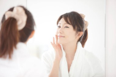 Genç Japon kadın banyoda aynaya bakıyor.