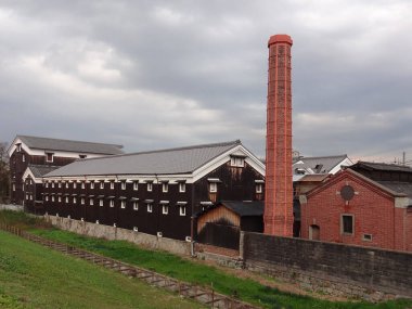 Açık havada uzun kırmızı tuğlalı baca bulunan tarihi sanayi binaları.