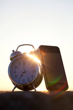 Gün batımında kumsalda çalar saatin ve akıllı telefonun yakın görüntüsü          