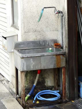 Yıpranmış metal lavabo boyalı duvarın önünde duruyor. 