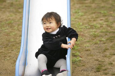 Küçük tatlı Asyalı kız çocuk oyun parkında kaydırak oynuyor.