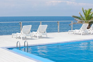 Güneş yatakları ve mavi deniz manzaralı boş yüzme havuzu alanı 