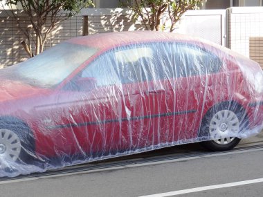 Dışarıdaki kırmızı araba şeffaf plastik çarşaf ile kaplanmış.