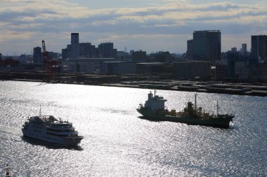 İki gemi şehrin ufuk çizgisi yakınlarında parıldayan sularda yüzüyor.