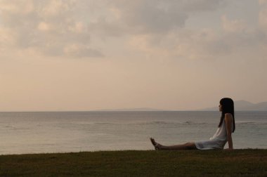Asyalı kadın sahilde oturuyor ve denizi izliyor.