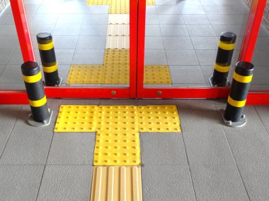 Sarı dokunsal asfalt cam giriş kapılarına doğru yol gösteriyor.