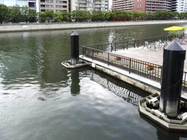 Açık nehir kenarı verandasında metal parmaklıklar ve boş masalar var.