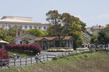 İnsanlar nehir kenarındaki patikada yürüyorlar. Çiçek açan çalıların ve ağaçların yanında.