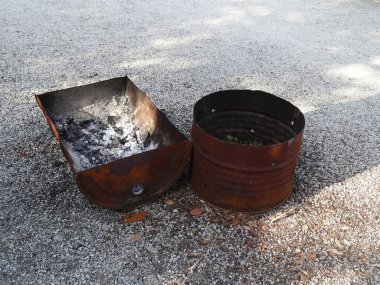 Paslı metal variller dışarıda, çakıl yüzeyinde duruyor.