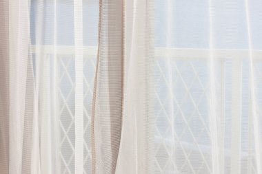 Balkon penceresindeki beyaz perdelerden süzülen güneş ışığı