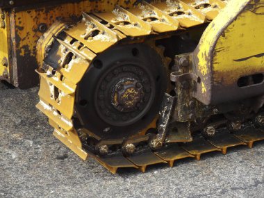 Yakından bakınca, kaba kaldırım yüzeyinde dinlenen sarı buldozer izlerini görüyoruz.