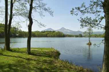 Gölü, yeşil ağaçları ve arka planda dağları olan güzel bir manzara.           