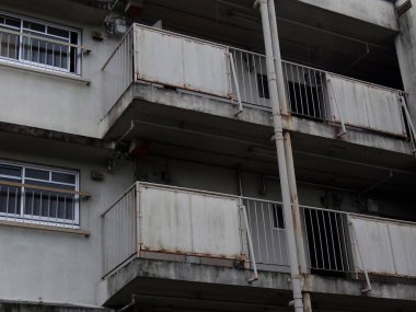 Paslı parmaklıkları ve lekeli beton yüzeyleri gösteren yıpranmış apartman balkonları.