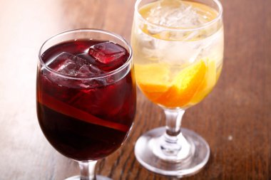 iki bardak buzlu kokteyl kırmızı şarap ve portakal dilimleri ahşap masada.