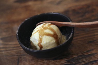 Ahşap masadaki siyah kasede lezzetli ve şuruplu dondurma manzarası.