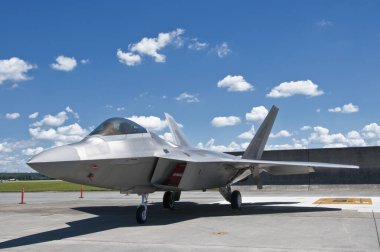 Askeri jet, açık mavi gökyüzünün altında, dağınık bulutların altında sergilendi.