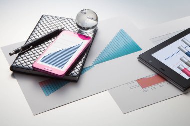 Beyaz arkaplanda akıllı telefon, dijital tablet, not defteri, kalem, cam küre ve iş haritalarının yakın plan görüntüsü     
