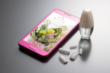 Cep telefonu ve kozmetik ürünlerinin yakın plan görüntüsü, gri arka planda tırnak cilası.          