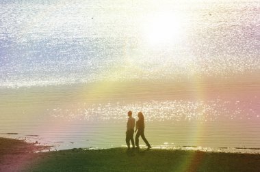 Gün batımında sahilde yürüyen çift.