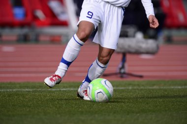 Bir futbolcu sahada futbol topunu tekmeliyor.