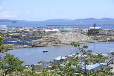 Büyük moloz yığınlarını çevreleyen sanayi binaları sakin suyun yanında.
