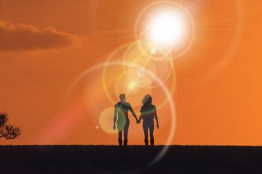 Gün batımına doğru el ele tutuşan kadın ve erkeğin silueti.