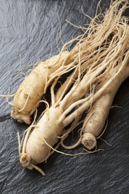 Siyah taş zemin üzerinde izole edilmiş üç ginseng kökü