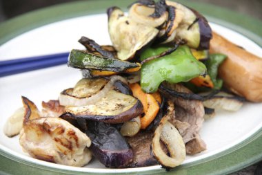 Grilled vegetables and meat resting atop white plate outdoors